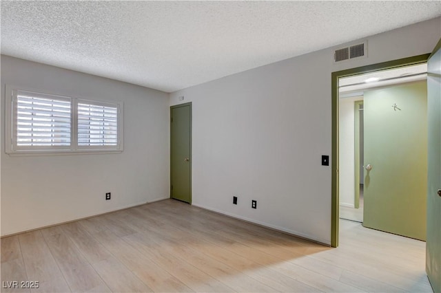 unfurnished room with light wood-style floors, visible vents, and a textured ceiling