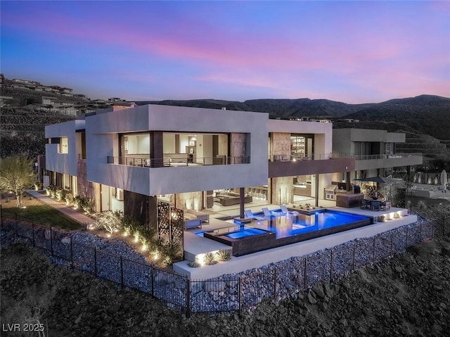 rear view of property with a pool with connected hot tub, stucco siding, a balcony, a patio area, and a mountain view