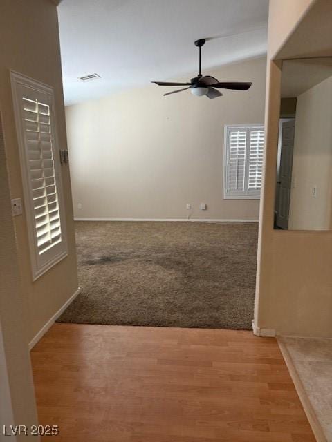 carpeted empty room featuring visible vents, baseboards, ceiling fan, vaulted ceiling, and wood finished floors