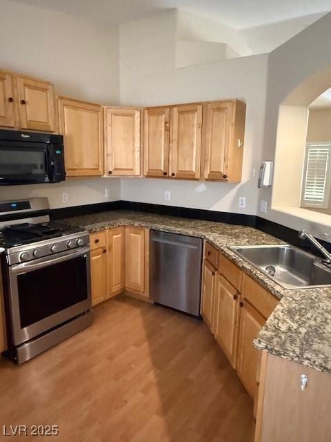 kitchen featuring light brown cabinetry, light wood finished floors, stainless steel appliances, and a sink