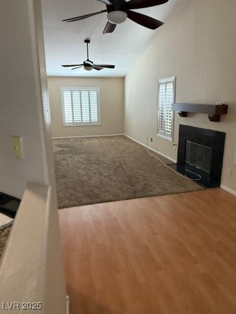 unfurnished living room featuring wood finished floors, a ceiling fan, carpet floors, lofted ceiling, and a glass covered fireplace