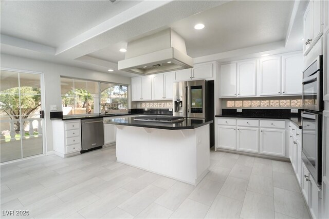 kitchen with premium range hood, a tray ceiling, dark countertops, appliances with stainless steel finishes, and white cabinets