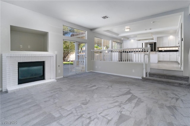 unfurnished living room featuring visible vents, a tray ceiling, carpet floors, a fireplace, and baseboards