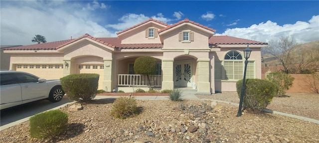 mediterranean / spanish house featuring a tile roof, a garage, covered porch, and stucco siding