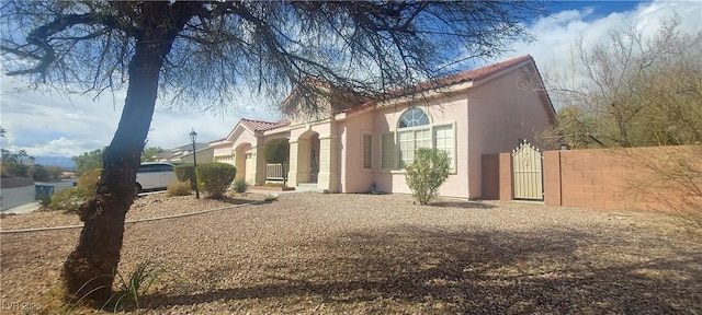 view of home's exterior featuring a tiled roof, a gate, fence, and stucco siding