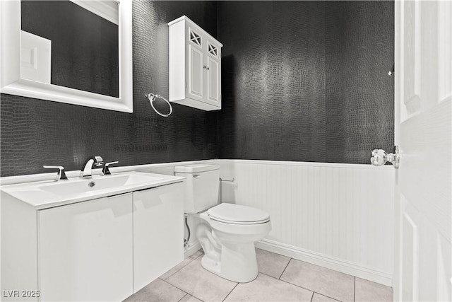 half bathroom featuring vanity, toilet, wainscoting, and tile patterned flooring