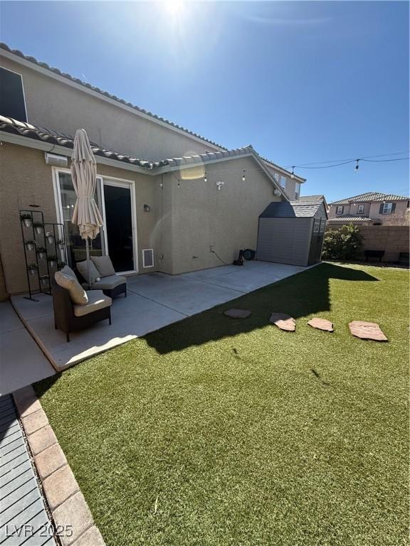 rear view of house featuring an outdoor structure, a storage unit, a patio area, and stucco siding