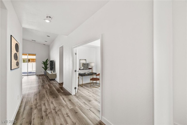 corridor with baseboards, lofted ceiling, visible vents, and light wood-style flooring