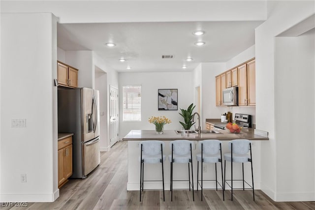 kitchen featuring visible vents, a peninsula, a kitchen breakfast bar, stainless steel appliances, and a sink