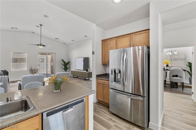 kitchen with light wood-type flooring, a sink, open floor plan, appliances with stainless steel finishes, and vaulted ceiling