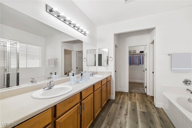 full bath with a sink, a garden tub, wood finished floors, and double vanity