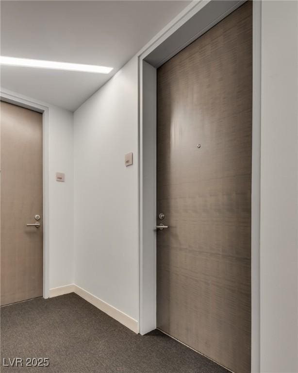 hall with baseboards and dark colored carpet