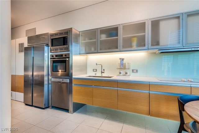 kitchen featuring light tile patterned flooring, a sink, light countertops, glass insert cabinets, and appliances with stainless steel finishes