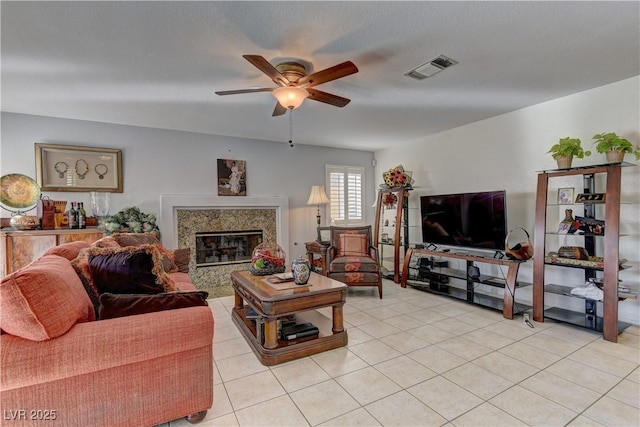 living room with light tile patterned floors, visible vents, a premium fireplace, and ceiling fan