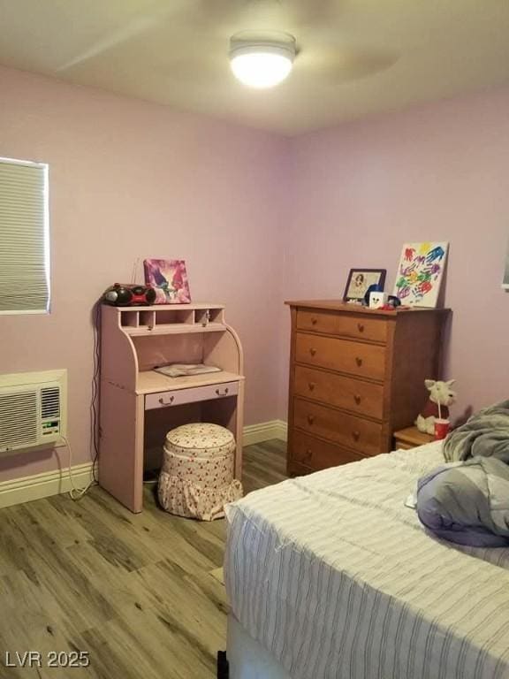 bedroom featuring a wall mounted air conditioner, baseboards, and wood finished floors