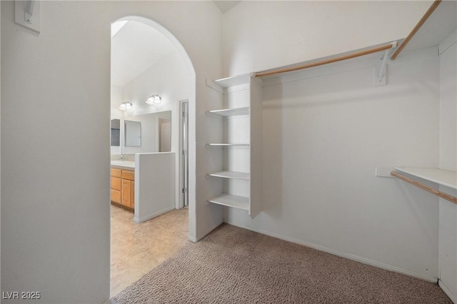 spacious closet featuring arched walkways and light colored carpet