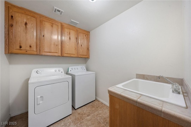 clothes washing area featuring washer and clothes dryer, visible vents, cabinet space, and a sink