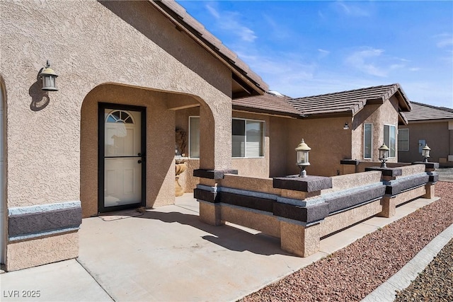 doorway to property featuring a patio, a tiled roof, and stucco siding