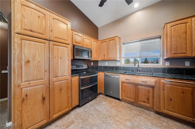 kitchen with tile counters, vaulted ceiling, stainless steel appliances, a ceiling fan, and a sink