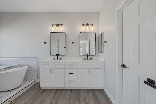 full bathroom featuring a freestanding bath, double vanity, wood finished floors, and a sink