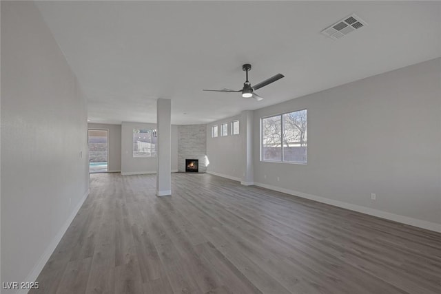 unfurnished living room with wood finished floors, visible vents, baseboards, a fireplace, and ceiling fan