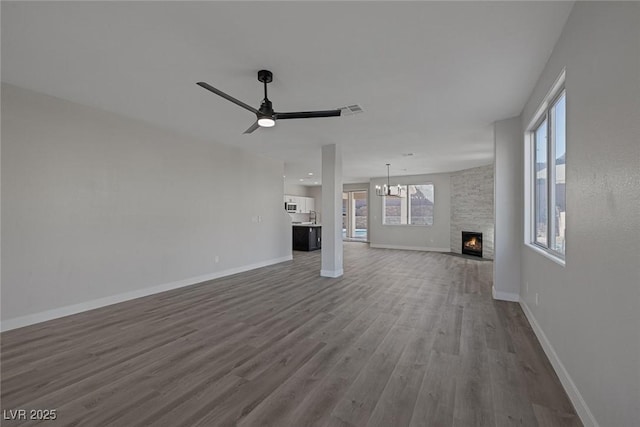 unfurnished living room with visible vents, ceiling fan with notable chandelier, dark wood finished floors, a fireplace, and baseboards