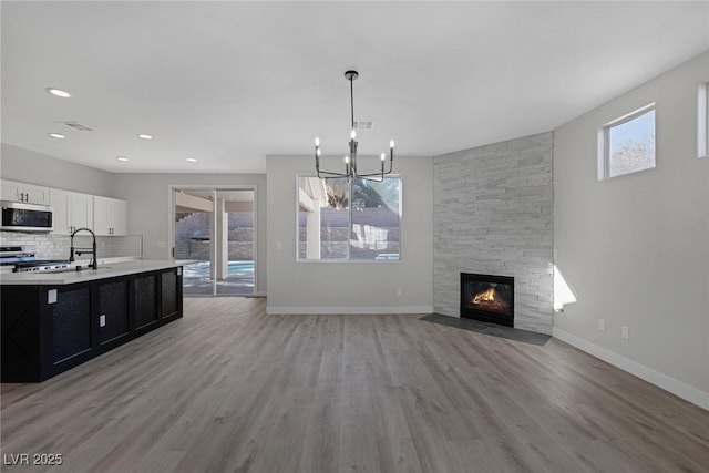 unfurnished living room with a stone fireplace, light wood-style flooring, an inviting chandelier, and baseboards