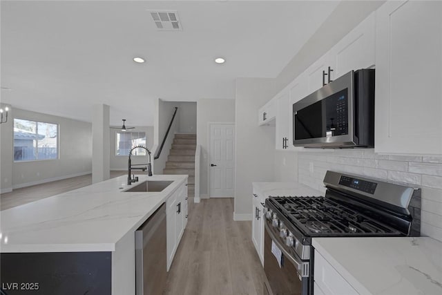 kitchen with light wood finished floors, visible vents, white cabinets, stainless steel appliances, and a sink