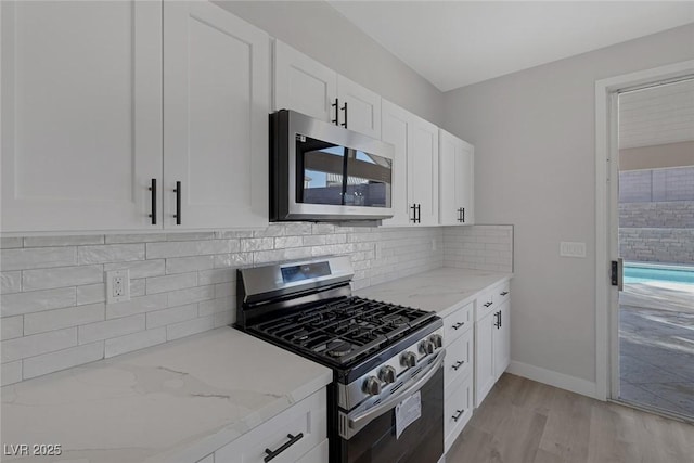 kitchen with light stone counters, tasteful backsplash, white cabinetry, stainless steel appliances, and light wood-style floors