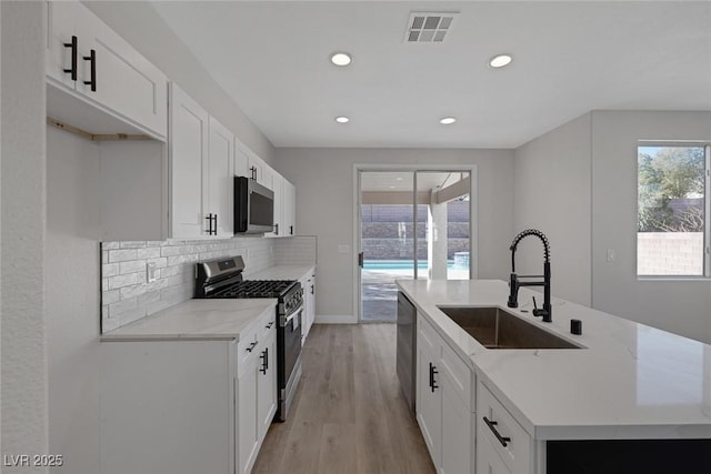 kitchen with visible vents, a kitchen island with sink, a sink, appliances with stainless steel finishes, and backsplash