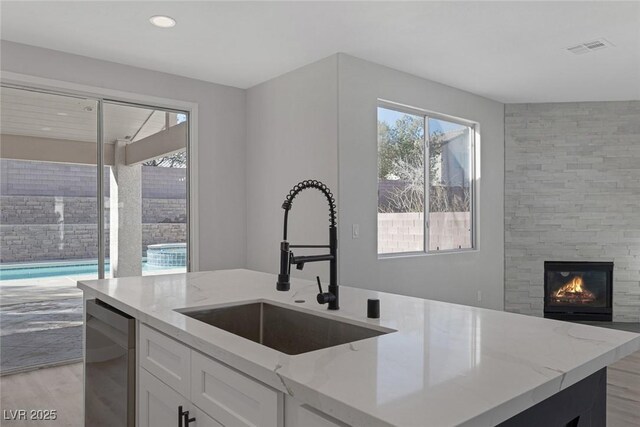 kitchen with a sink, a large fireplace, light stone countertops, and light wood-style flooring