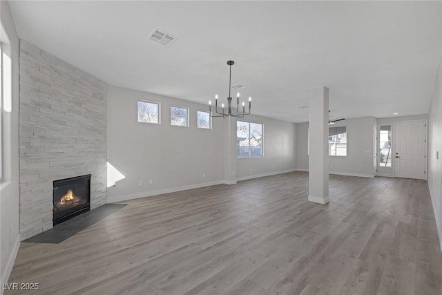 unfurnished living room featuring a stone fireplace, baseboards, visible vents, and wood finished floors