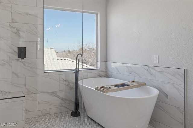 bathroom featuring a freestanding bath, tile walls, and a textured wall