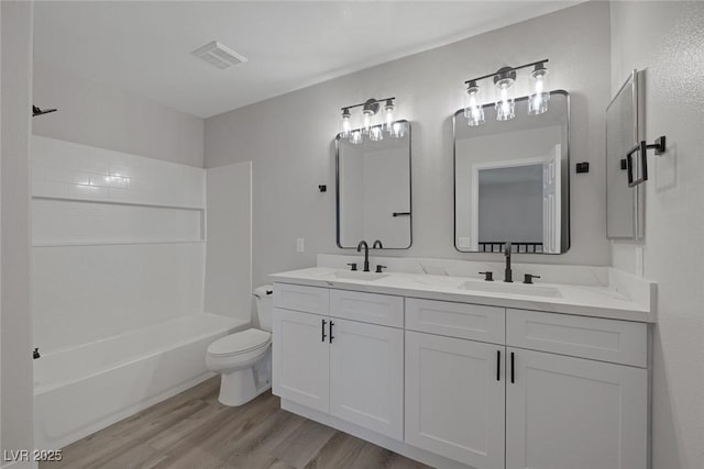 full bath with toilet, wood finished floors, visible vents, and a sink