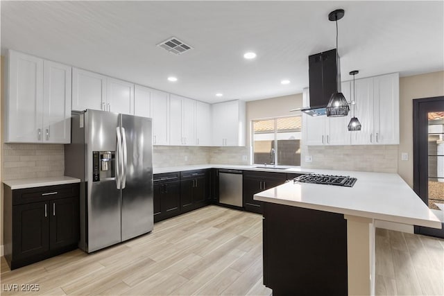 kitchen with light countertops, appliances with stainless steel finishes, island exhaust hood, a peninsula, and a sink