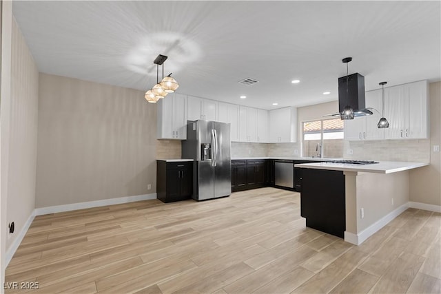 kitchen with visible vents, light countertops, a peninsula, island exhaust hood, and stainless steel appliances