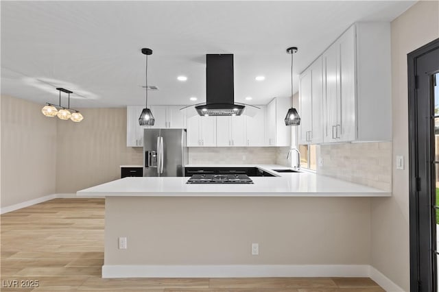 kitchen with a sink, stainless steel fridge, island range hood, and light countertops