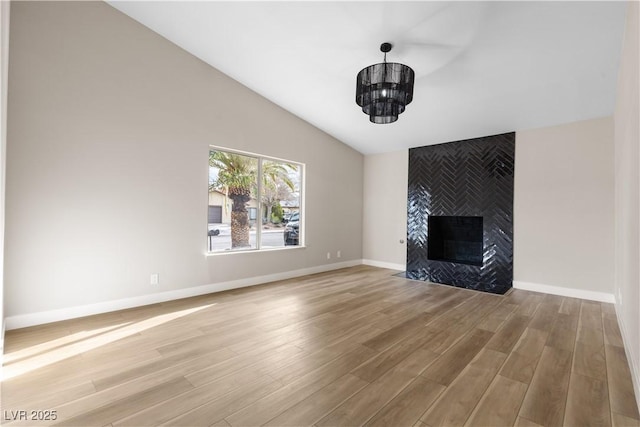 unfurnished living room with a notable chandelier, lofted ceiling, wood finished floors, baseboards, and a tile fireplace