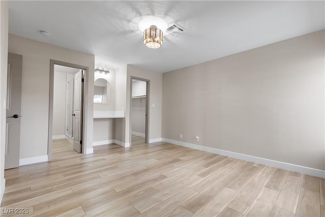 unfurnished bedroom featuring visible vents, a spacious closet, light wood-style floors, and baseboards