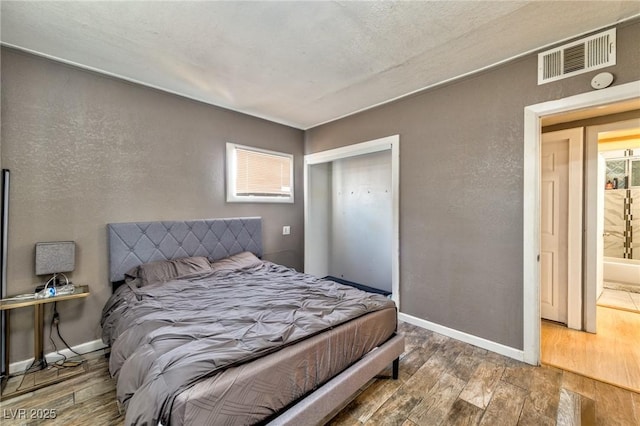 bedroom featuring visible vents, baseboards, wood finished floors, a textured wall, and a closet