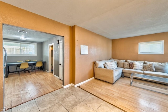 living area with light wood-type flooring, visible vents, baseboards, and a textured ceiling