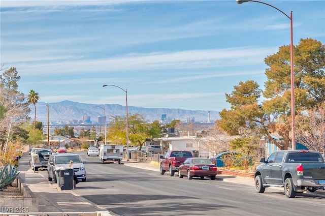 view of street with sidewalks, a mountain view, curbs, and street lights