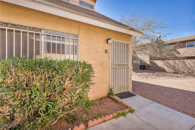 entrance to property with stucco siding, central AC, and fence