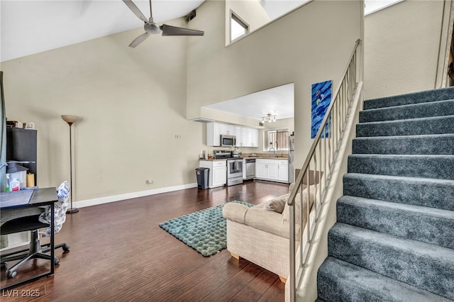 living room featuring a ceiling fan, baseboards, high vaulted ceiling, stairs, and dark wood-type flooring