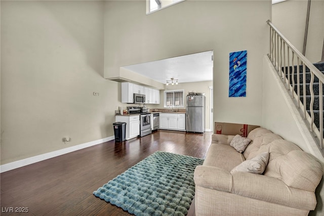 living area with a high ceiling, stairs, dark wood-type flooring, and baseboards