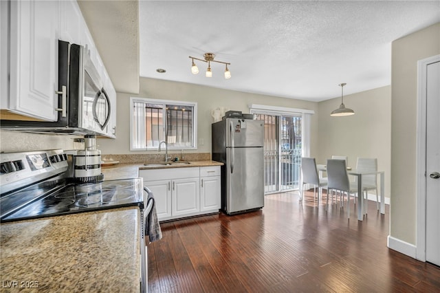 kitchen with dark wood-type flooring, light stone countertops, stainless steel appliances, white cabinetry, and a sink