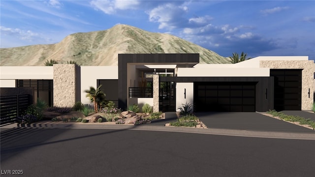 contemporary house featuring stucco siding, fence, a mountain view, concrete driveway, and an attached garage