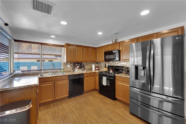 kitchen with a sink, visible vents, backsplash, and black appliances