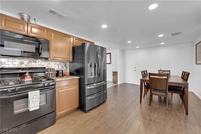 kitchen featuring light wood finished floors, visible vents, black appliances, and decorative backsplash