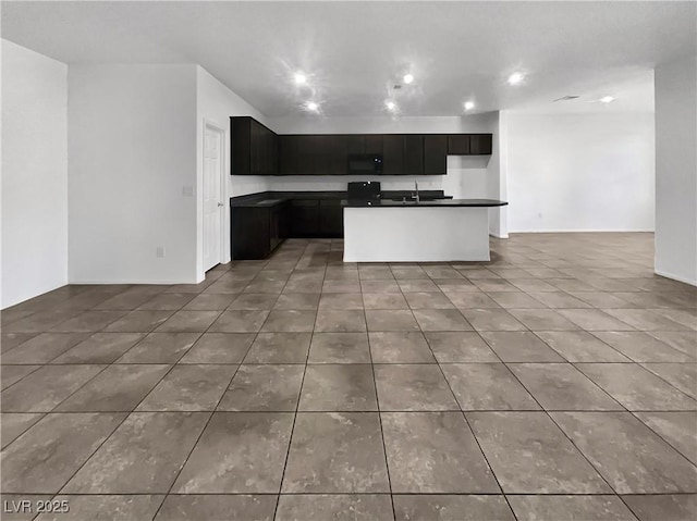 kitchen featuring tile patterned floors, dark countertops, open floor plan, black microwave, and dark cabinets